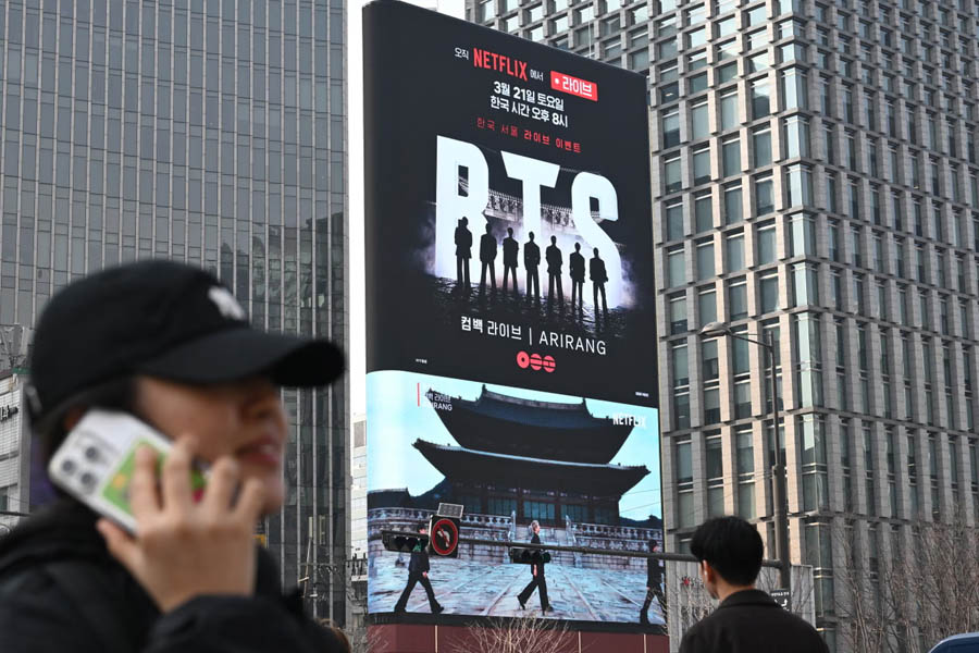 People passing a large BTS comeback concert billboard at Gwanghwamun Square in Seoul, highlighting anticipation for the K-pop group’s return event.