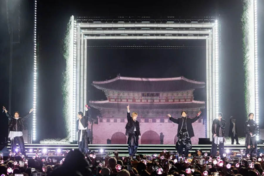 BTS on stage at Gwanghwamun Gate in Seoul with fans and light sticks surrounding the historic palace gate.