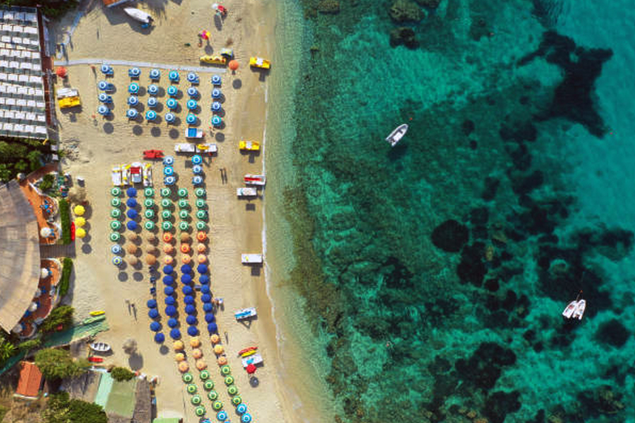 Aerial top down view of Capo Vaticano beach in Calabria, Italy showing umbrellas and boats in crystal clear water