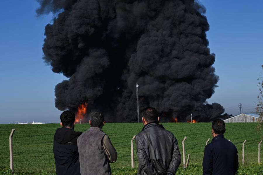 People watch as smoke billows from an oil warehouse in the Kani Qirzhala area on the outskirts of Erbil, the capital of Iraq's autonomous Kurdistan region, following a suspected drone strike.
