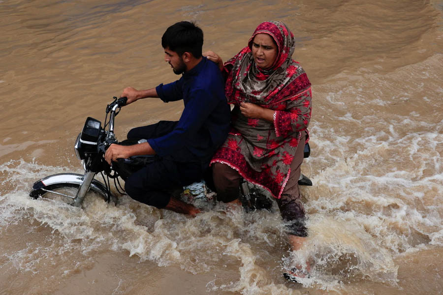 Two people on a motorbike navigating a flooded road in Sialkot, Pakistan, during severe monsoon flooding.