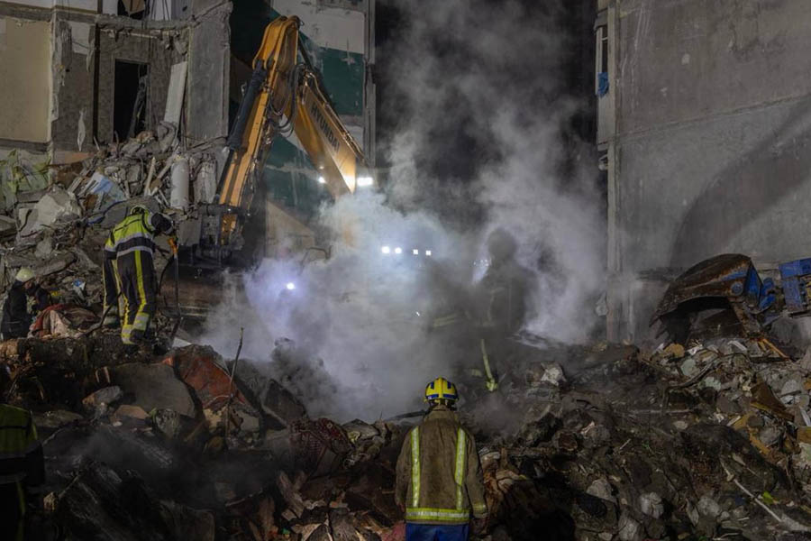 Rescue workers climb through the debris of a nine-story residential building in Kyiv that was partially destroyed by a Russian missile strike, as search operations continue for missing residents.