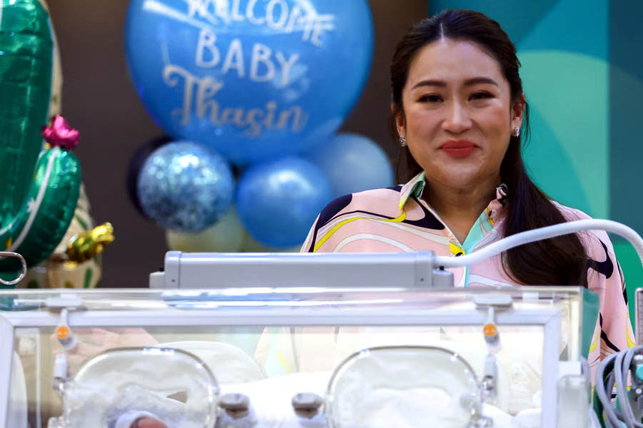 Paetongtarn Shinawatra stands beside an incubator holding her newborn baby during a 2023 news conference in Bangkok, symbolizing the merging of new life and new political beginnings.