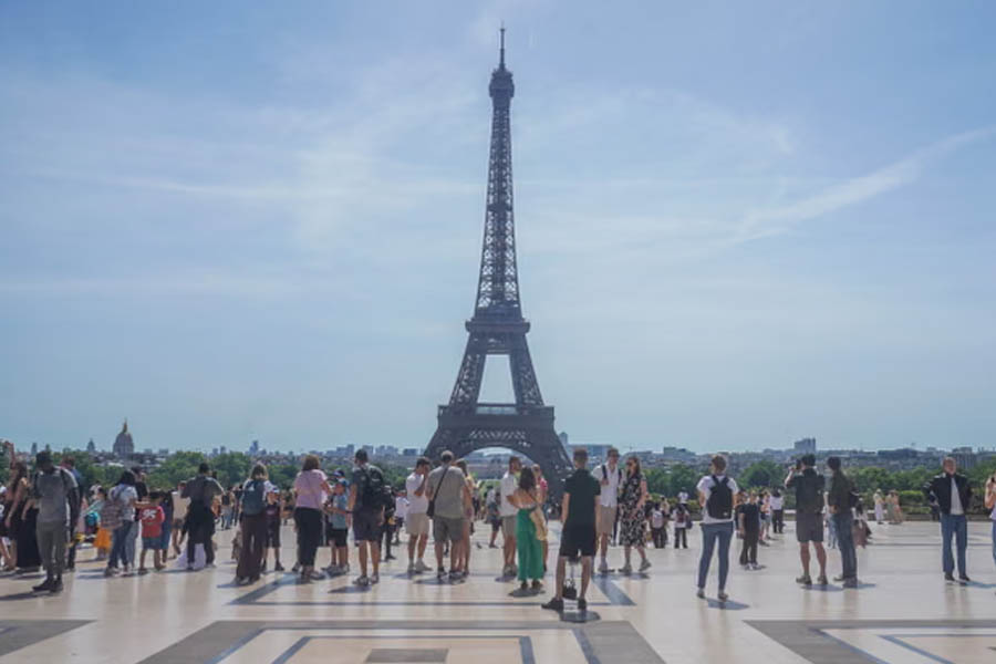 Crowds of tourists at the Trocadero Gardens looking at the Eiffel Tower on a hazy, sweltering summer day in Paris.