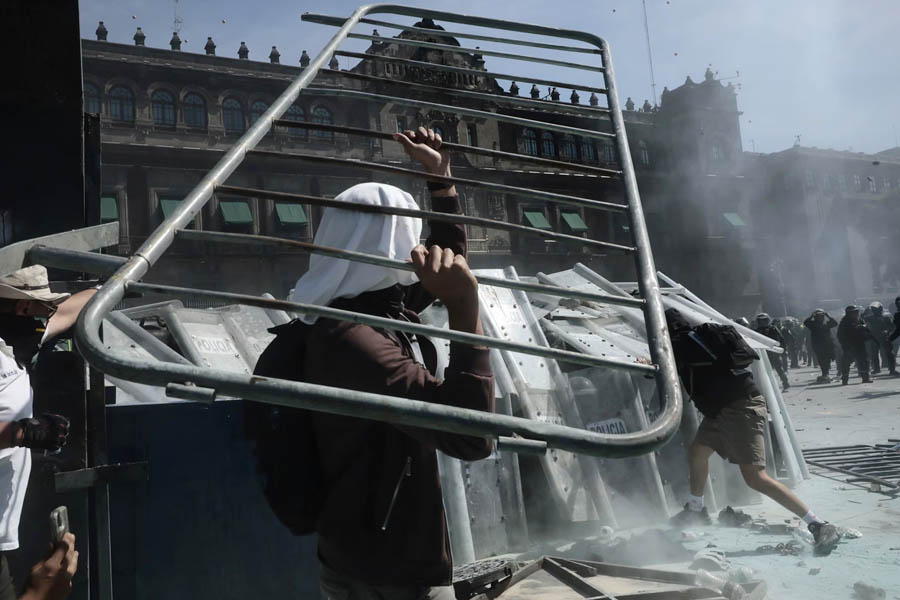 Protesters confronting police and breaking barricades near the National Palace in Mexico City during a violent demonstration.