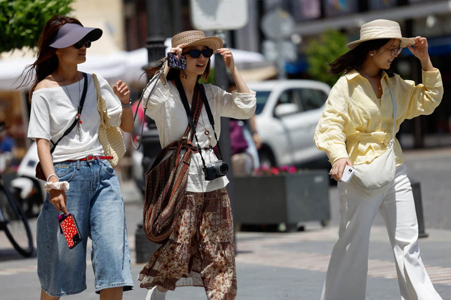 Tourists using umbrellas and fans to shield themselves from the intense sun while visiting the historic town of Ronda, Spain, during a severe heatwave.