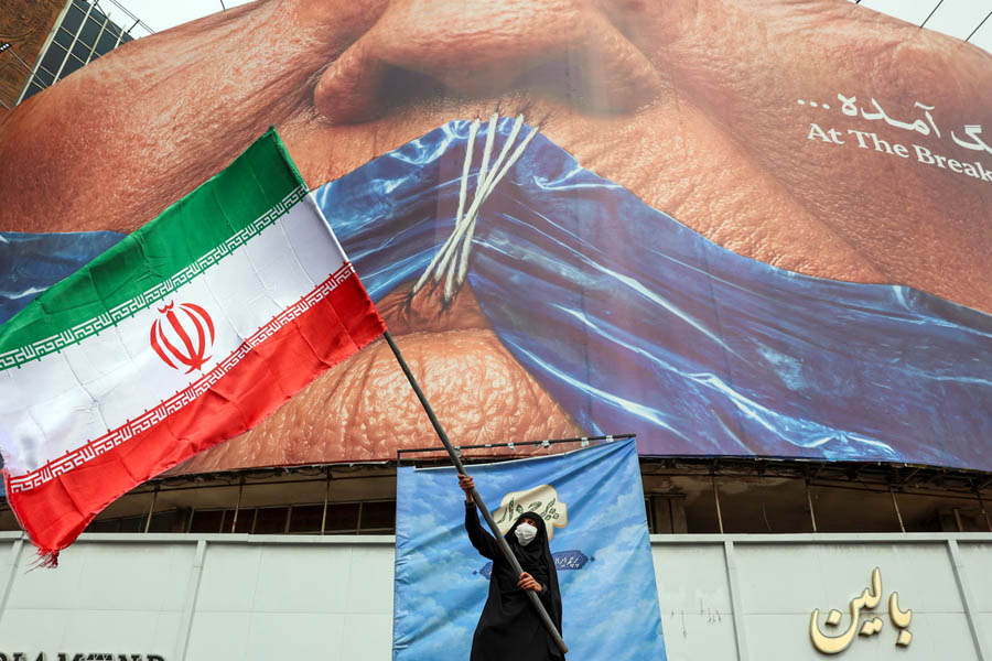 A woman waves an Iranian flag in front of an anti-US billboard referring to Donald Trump and the Strait of Hormuz in Tehran.