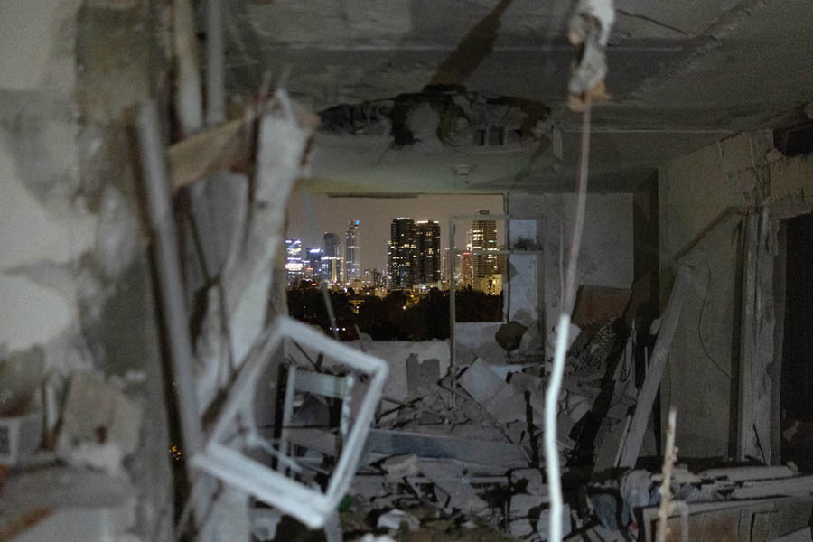 Damaged residential building in Tel Aviv after Iranian missile strike, with destroyed facade, debris scattered, and emergency responders at the scene