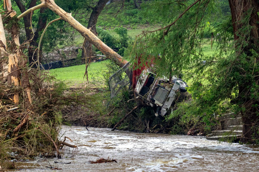 A truck is pierced by a fallen tree on the flooded banks of the Guadalupe River in Center Point, Texas, as deadly flash floods claim over 100 lives — including 27 from Camp Mystic — with more rain threatening the region.
