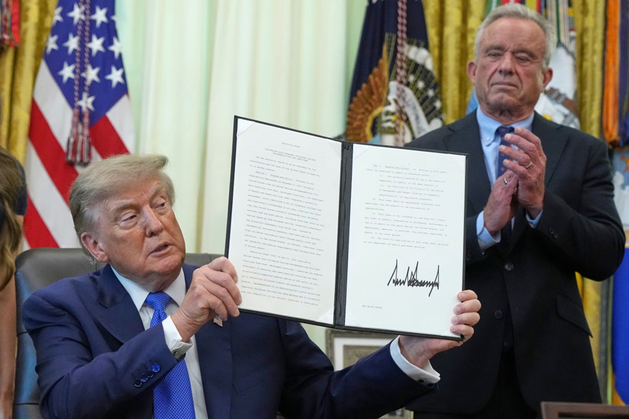 Donald Trump holds a signed executive order about vaccines as Health and Human Services Secretary Robert F. Kennedy Jr. looks on