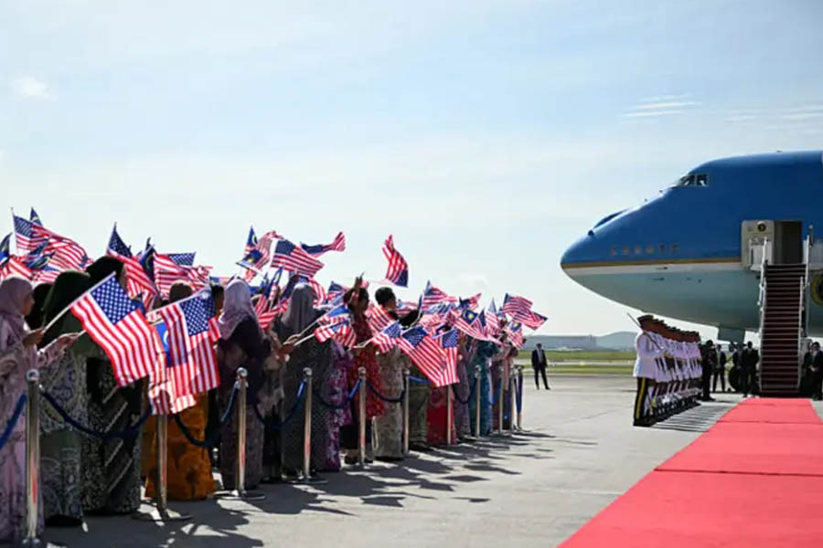 Donald Trump smiling and waving U.S. and Malaysian flags as he is greeted by dancers and supporters during a fanfare-filled welcome ceremony in Kuala Lumpur.