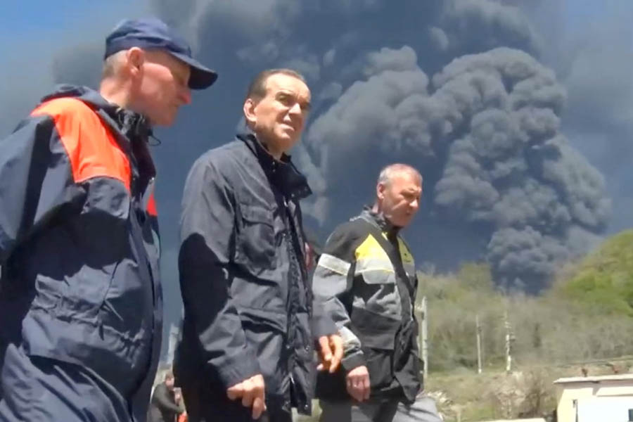 Russian officials in Tuapse stand against the backdrop of thick smoke rising from the burning oil refinery after another Ukrainian drone strike.
