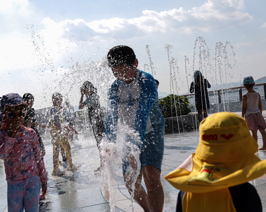 Children cool off in a water fountain at a Hong Kong park as the city reaches a record temperature of 36.9C