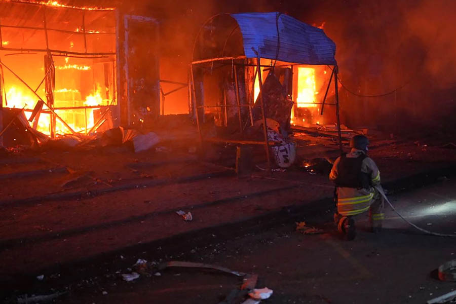 Ukrainian rescuer extinguishing a large fire amid destroyed buildings in Zaporizhzhia after an attack that killed five and injured three.