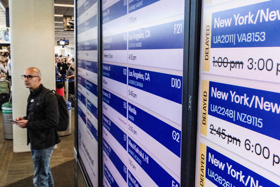 Passenger viewing flight delay information on an airport screen at San Francisco International Airport amid U.S. government shutdown flight disruptions.
