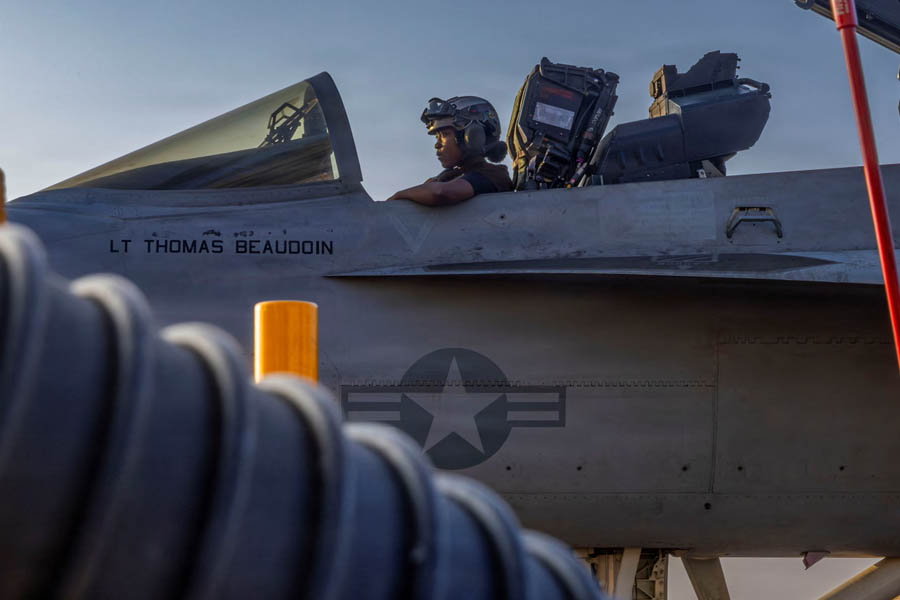US Navy crew members conducting maintenance work on an F/A-18E Super Hornet fighter jet on the flight deck of the USS Abraham Lincoln in the Arabian Sea.