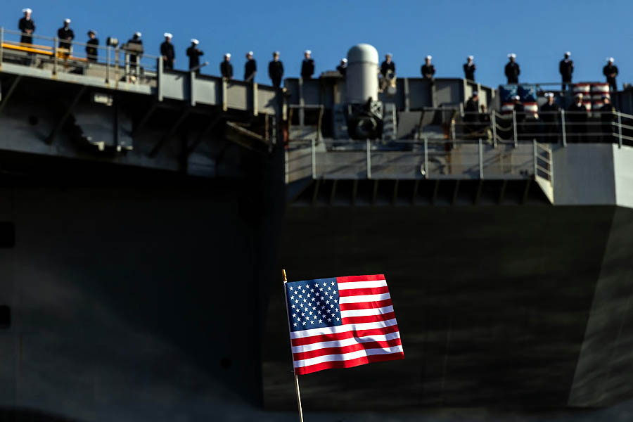 An American flag is waved as sailors stand at the rails while the USS George HW Bush prepares for deployment on Tuesday.